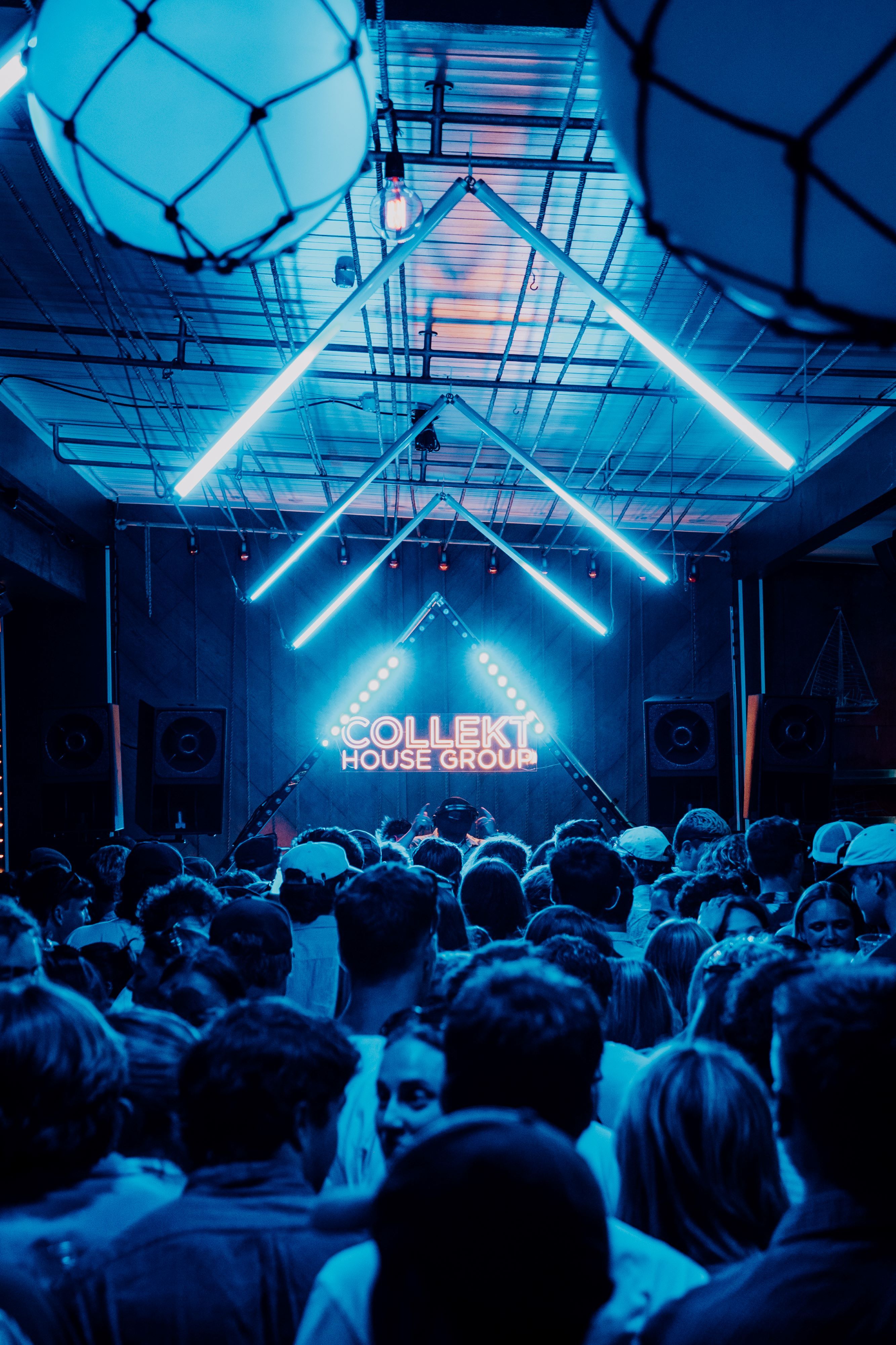 A long narrow venue, lit by blue neon bars, the 'collekt' logo is lit up on the stage in front of the crowd